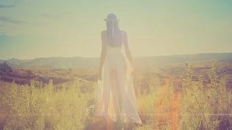 Back view of the beautiful woman in white dress, among the colorful fields, on the mountains