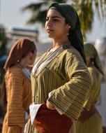 Greek Cypriot woman with the traditional head kerchief, near the people and palm tree