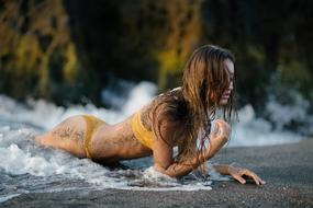 Beautiful girl in yellow swimsuit, laying on the sandy beach, near the colorful rocks