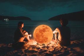 couple sitting on the beach by the glowing moon at night