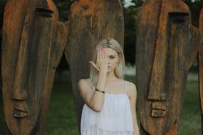 Blonde girl closing her half of the face with her hand near the statues