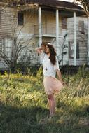 Posing woman in white and orange clothing, and in hat, on the beautiful green grass field, near the house