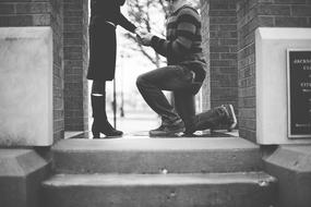 monochrome photo of unrecognizable man kneeling in front of woman on steps