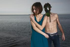 man in gas mask behind young girl at sea