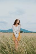 Posing, smiling girl, on the beautiful, yellow and green grass meadow, near the mountains