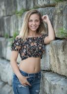 Smiling, blonde teen in jeans, near the stone wall, with the green plants