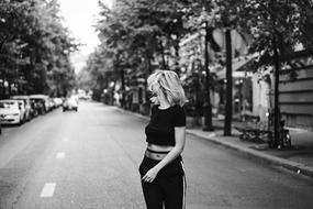 Black and white photo of the beautiful girl on the road, with cars, among the trees and buildings