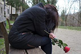 Sad girl with red rose flower sitting on the bench