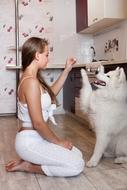 Girl in white clothing, near the beautiful and cute, white, fluffy dog in the kitchen