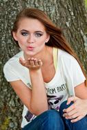 Portrait of a woman with make-up, blowing a kiss, near the tree