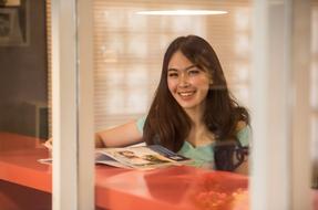 Smiling Asian girl reading a magazine on a red table