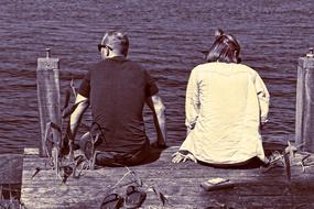 black and white photo of husband and wife sitting on a wooden pier on the lake