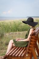 a girl in a black hat sits on a wooden bench