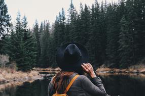 woman in black hat near forest lake