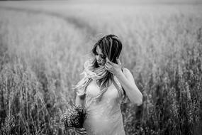 young pregnant woman stands with bouquet in front of field