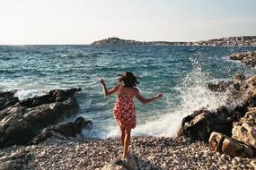 joyful girl in a floral dress on the shore of a rocky ocean beach