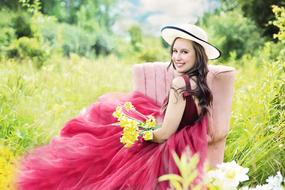 Pretty woman with the flowers and hat on the landscape