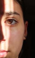 Half face of the woman, with brown eye, in light and shadow, at black background