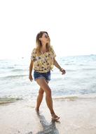 Woman in sunglasses and jeans short, walking on the beautiful, sandy beach in light