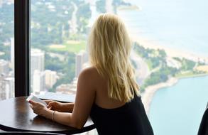 Back view of a blonde girl in black dress, looking on the beautiful shore, through the window