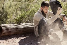 Guy in Fashion clothing sits on soil with hat in hand