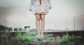 Legs of the woman with colorful, patterned drees, on the railroad with green plants