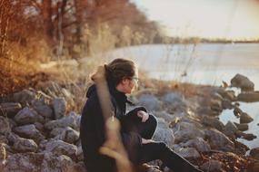 young girl sits Alone on rocky coast at fall