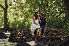 couple in love sits on the roots of a tree
