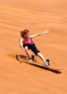 Sandboarding, young girl speeding on dune