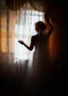 a girl in a wedding dress stands by the window