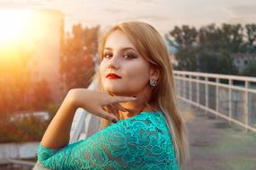 Portrait of the beautiful, blonde woman, with the make-up and earrings, in turquoise dress, on the bridge, in the colorful sunset