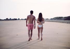 Man and Woman in bikini walking away on beach