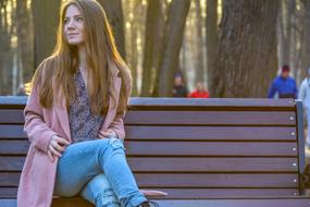 Smiling girl, sitting on the wooden bench, near the trees in the park