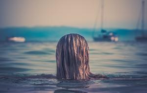 Back view of the woman, with the wet hair, near the boats on the water, at colorful sunset