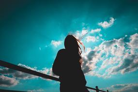 silhouette of a girl on a bridge against a blue sky with white clouds