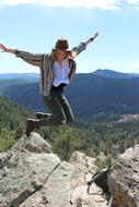 Beautiful, blonde woman in hat, jumping on the rocks, on the beautiful, green mountains