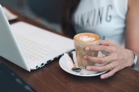 Woman, with the glass of coffee with beautiful heart drawing, near the white laptop
