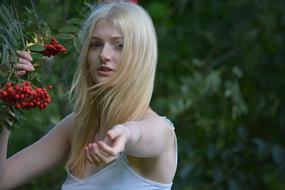 Portrait of the beautiful, blonde young woman, near the red berries, showing hand