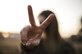 Close-up of the girl, showing peace sign, at blurred background with light