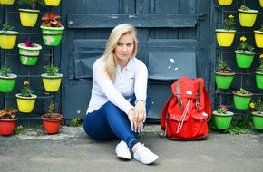 blonde with a red backpack posing on the background of potted plants