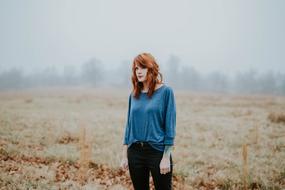 red haired Woman in blue blouse and black pants posing on meadow
