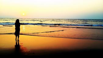 Back view with the silhouette of a woman, on the beautiful, sandy beach, at colorful sunset on horizon