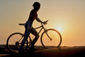 female Cyclist walking with bike at sunset
