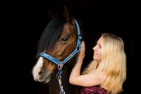 Smiling, blonde woman, with the beautiful and cute, brown and white horse, at black background