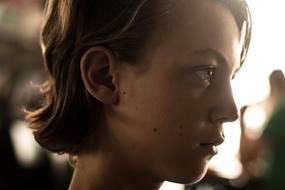 Profile portrait of the young girl, with the short hair, at blurred background with the sunlight