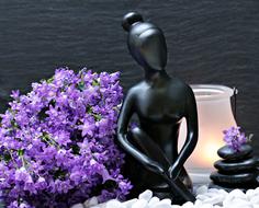 Beautiful, black woman sculpture among the purple flowers, white and black stones, near the beautiful candle