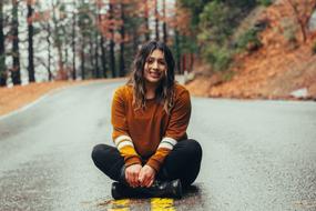 Smiling, beautiful girl, sitting on the beautiful, wet road, among the colorful trees, in the autumn