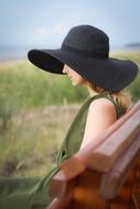 girl in wide black hat sits on bench at Summer