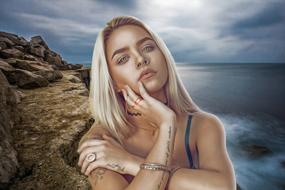 Portrait of the posing, blonde woman with the tattoo, on the beautiful, rocky coast, under cloudy sky