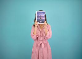 Woman in pink gown holding a book at face at blue background
